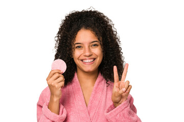 Young african american woman wearing a pink bathrobe holding a cellulose disk showing number two...