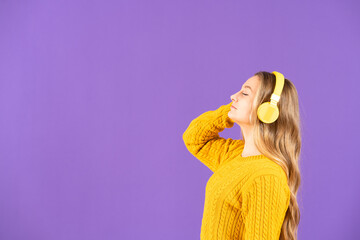 Side view of young woman listening to music on headphones isolated on purple background with copy space