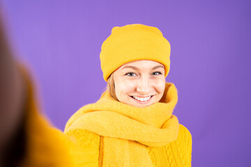 Selfie portrait of pretty woman wearing yellow winter clothes isolated on purple background