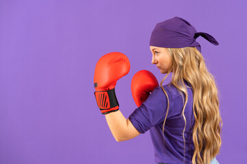 Side view of feminist pretty woman wearing boxing gloves isolated on purple background. Feminism...