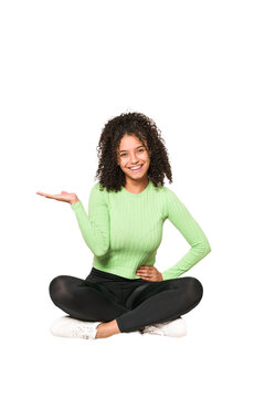 Young African American Curly Woman Sitting On The Floor Isolated