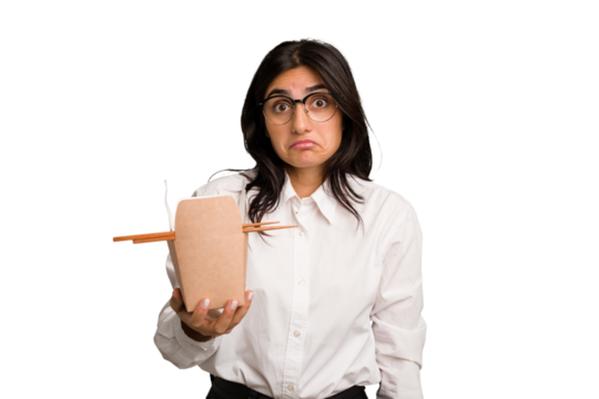 Young business indian woman eating takeaway noodles cut out isolated shrugs shoulders and open eyes confused.