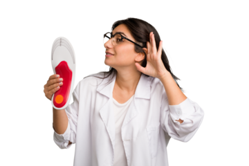 Young indian chiropodist woman holding a insoles for shoes cut out isolated trying to listening a gossip.
