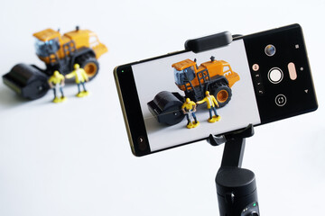 Smartphone on a gimbal selfie stick for photo-video, filming toy construction machinery and workers. Concept of live broadcast construction, video blogging, podcasts, streaming and journalism. - obrazy, fototapety, plakaty