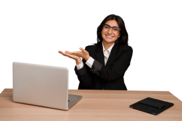 Young indian woman in a table with a laptop and tablet isolated holding a copy space on a palm.