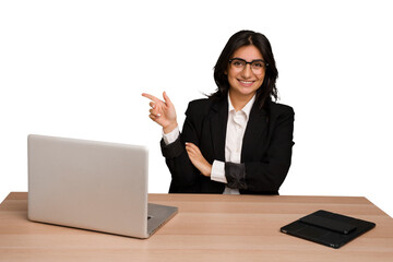 Young indian woman in a table with a laptop and tablet isolated smiling cheerfully pointing with...