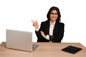 Young indian woman in a table with a laptop and tablet isolated smiling cheerfully pointing with forefinger away.