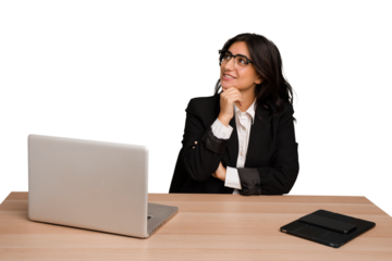 Young indian woman in a table with a laptop and tablet isolated looking sideways with doubtful and skeptical expression.