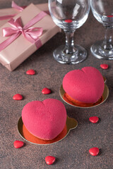 Homemade bright mousse cakes Hearts with pink velor coating, two glasses and champagne for Valentine's Day