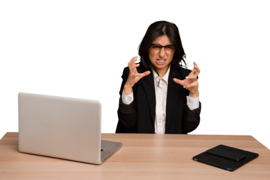 Young indian woman in a table with a laptop and tablet isolated upset screaming with tense hands.