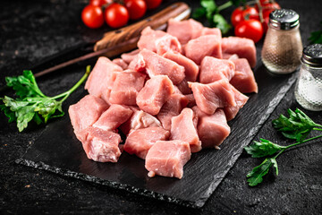Pieces of raw pork on a stone board with parsley, tomatoes and spices. 