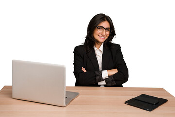 Young indian woman in a table with a laptop and tablet isolated who feels confident, crossing arms...