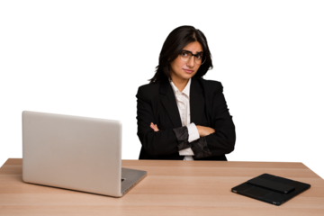 Young indian woman in a table with a laptop and tablet isolated suspicious, uncertain, examining you.