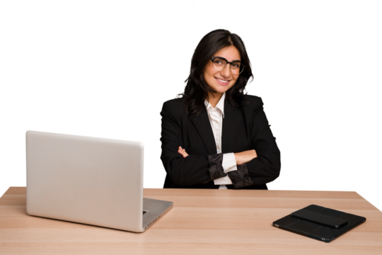 Young indian woman in a table with a laptop and tablet isolated who feels confident, crossing arms with determination.
