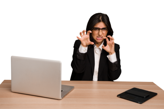 Young indian woman in a table with a laptop and tablet isolated showing claws imitating a cat, aggressive gesture.