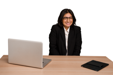 Young indian woman in a table with a laptop and tablet isolated laughs and closes eyes, feels relaxed and happy.