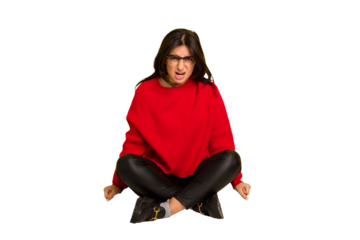 Young indian woman sitting on the floor cut out isolated shouting very angry, rage concept, frustrated.