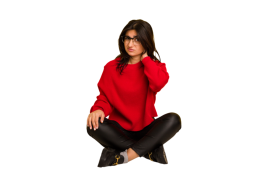 Young indian woman sitting on the floor cut out isolated touching back of head, thinking and making a choice.