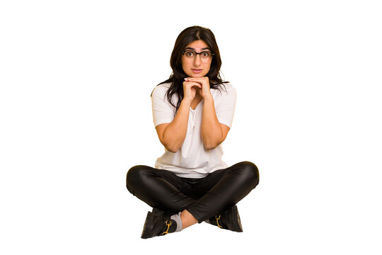Young indian woman sitting on the floor cut out isolated praying for luck, amazed and opening mouth looking to front.