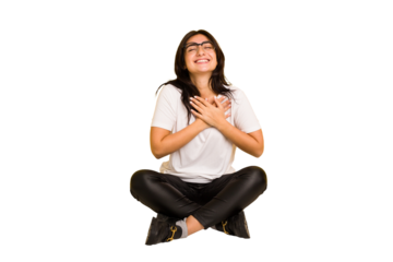 Young indian woman sitting on the floor cut out isolated laughing keeping hands on heart, concept of happiness.