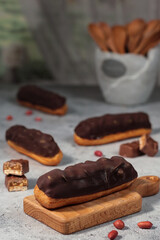 Classic chocolate-covered éclairs, their glossy tops hiding the rich, creamy filling inside, presented on a simple wooden surface.