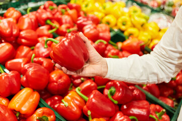 Hand eines Kunden hält rote Paprika beim Einkaufen