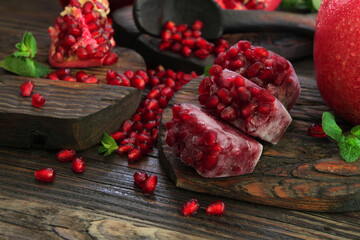 Ripe pomegranate, red, cut, sweet with beautiful grains, aesthetically laid out on a wooden table and decorated with green mint, sauce and juice are poured into bottles nearby.