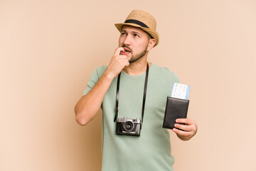 Young latin man holding flight tickets isolated relaxed thinking about something looking at a copy space.