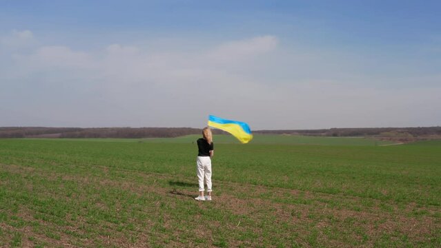 A blonde woman waving Ukrainian flag on a field horizon background. Around panorama view. A flag is on a flag stock. High quality 4k footage