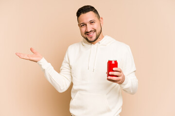 Young latin man holding a cola refreshment isolated showing a copy space on a palm and holding...