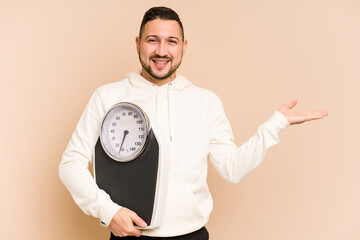 Adult latin man holding a weight scale isolated showing a copy space on a palm and holding another...