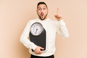 Adult latin man holding a weight scale isolated having some great idea, concept of creativity.