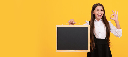 surprised child in uniform hold school blackboard for copy space showing ok gesture, advertising....