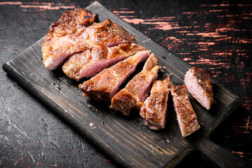 Slices of grilled steak pork on a wooden cutting board. 