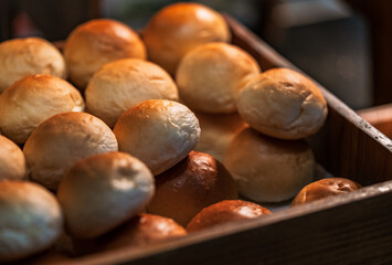 Close-up hot Fresh Baked Bread Rolls in a wooden box for the customer, the stack of freshly baked bread rolls, warm light from above.