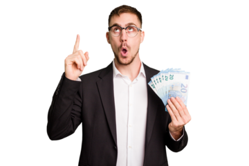 Young business caucasian man holding euro banknotes isolated cut out pointing upside with opened mouth.