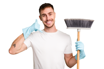 Young man holding a broom to clean his house cut out isolated showing a mobile phone call gesture with fingers.