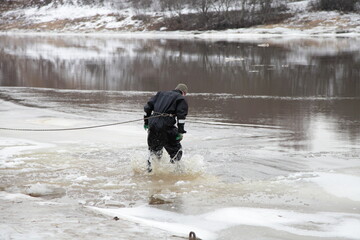 Rescue diver dives from the ice into the water for rescue on a river in winter