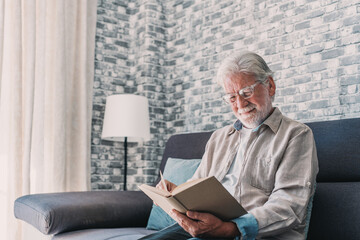 Headshot portrait close up of old happy and relaxed man sitting reading a book at home. Mature male...