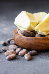Cocoa butter or Cocoa bean solid oil with cacao powder in spoon and raw cocoa beans on rustic backdrop, healthy natural oil