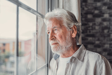 Pensive elderly mature senior man in eyeglasses looking in distance out of window, thinking of...