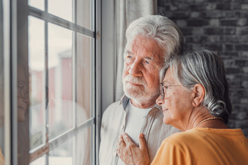 Obraz na płótnie Canvas Pensive elderly mature senior man in eyeglasses looking in distance out of window, thinking of personal problems. Old woman wife consoling and hugging sad husband, copy space.