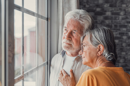 Pensive elderly mature senior man in eyeglasses looking in distance out of window, thinking of personal problems. Old woman wife consoling and hugging sad husband, copy space.