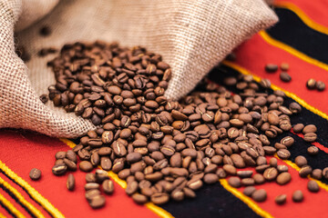 Roasted coffee beans or seeds in a jute sack and scattered on a tablecloth with African...