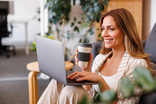 Female web designer drinking coffee and using laptop computer
