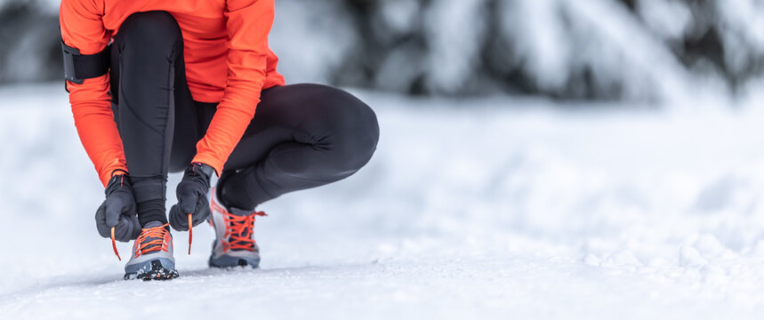 An attractive female runner is tying her shoelaces before training on the snow in the winter season.