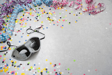 Karnevalsmaske auf grauem Hintergrund mit bunten Konfetti und Luftschlangen