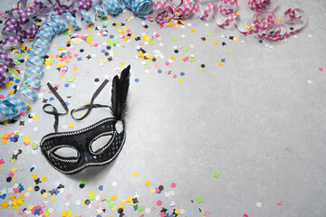 Venezianische Karnevalsmaske auf grauem Hintergrund mit bunten Konfetti und Luftschlangen