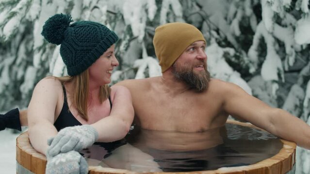 Caucasian couple sitting in wooden barrel with frozen water. Shot with RED helium camera in 8K.  