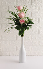 Modern spring party composition made of white champagne bottle and bouquet of pink rose flowers on the table. White party background. Valentine's Day concept.